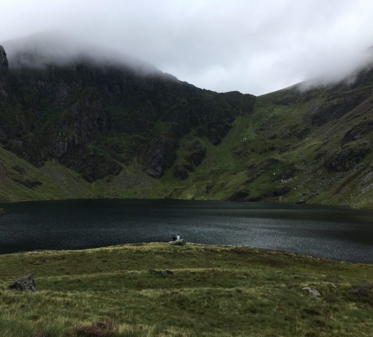 Llyn Cau Tranquil lake surrounded by rocky cliffs and misty mountains under a cloudy sky.